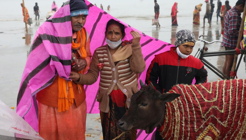 Hindu pilgrims cover themselves with a plastic sheet during rainfall as pilgrims gather at the confluence of the river Ganges and the Bay of Bengal on the occasion of 